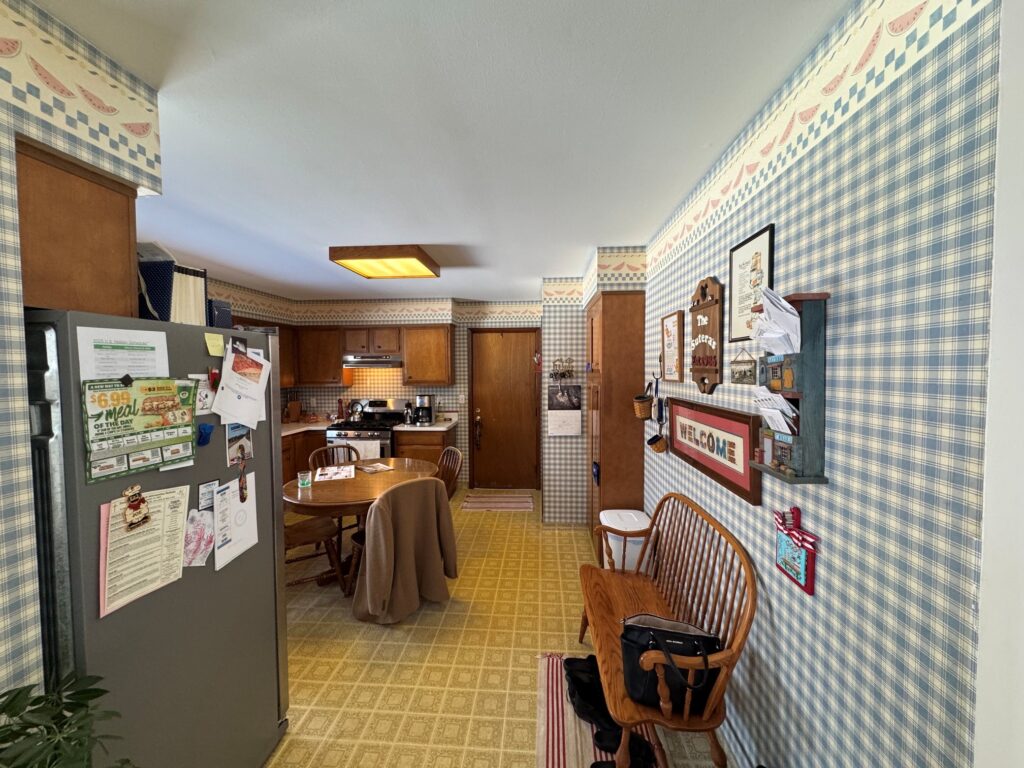 Before kitchen remodel in Harvard IL featuring outdated wallpaper, linoleum flooring, and original Wood Cabinetry