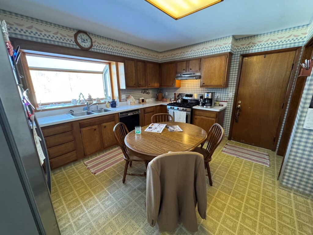Before kitchen remodel in Harvard IL with outdated cabinets, wallpaper, and linoleum flooring