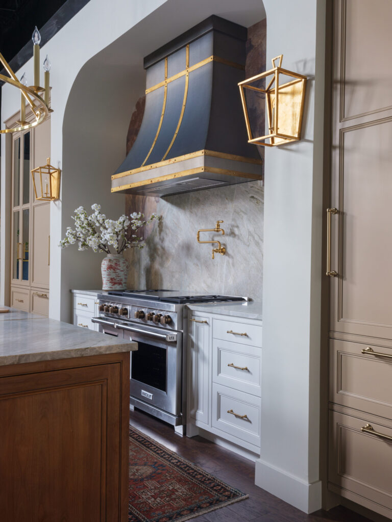 Custom decorative range hood with brass accents above luxury cooking area featuring Stratford inset cabinetry by Mouser Cabinetry.