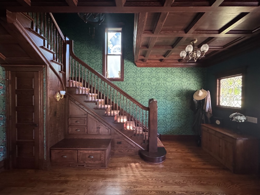 Historic first floor remodel in Woodstock, IL featuring restored wood staircase, coffered ceiling, hardwood flooring, custom millwork, and decorative wallpaper by CSL Interior.