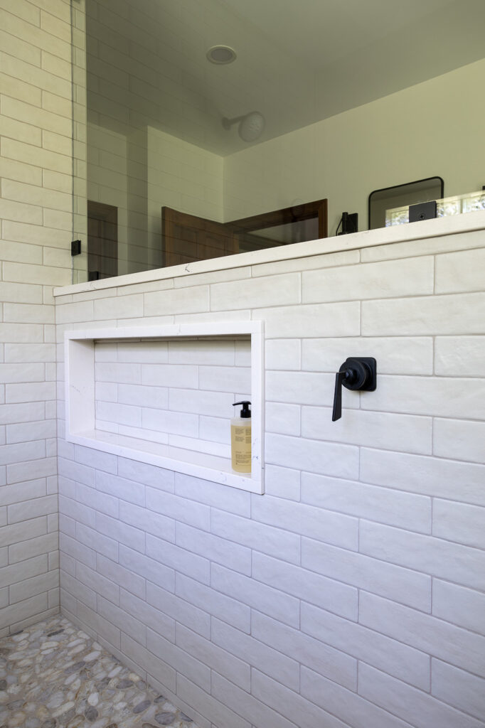 Custom recessed shower niche featuring Ragno Calce 3 x 11 Panna wall tile, California Faucets Steampunk Bay controls, and a pebble shower floor in a luxury master bathroom remodel in Woodstock, Illinois.