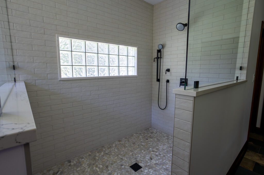 Custom spa-inspired walk-in shower with frameless glass, California Faucets Steampunk Bay shower system, Ragno Calce wall tile, pebble shower floor, and Marvin Elevate windows in Woodstock, Illinois.
