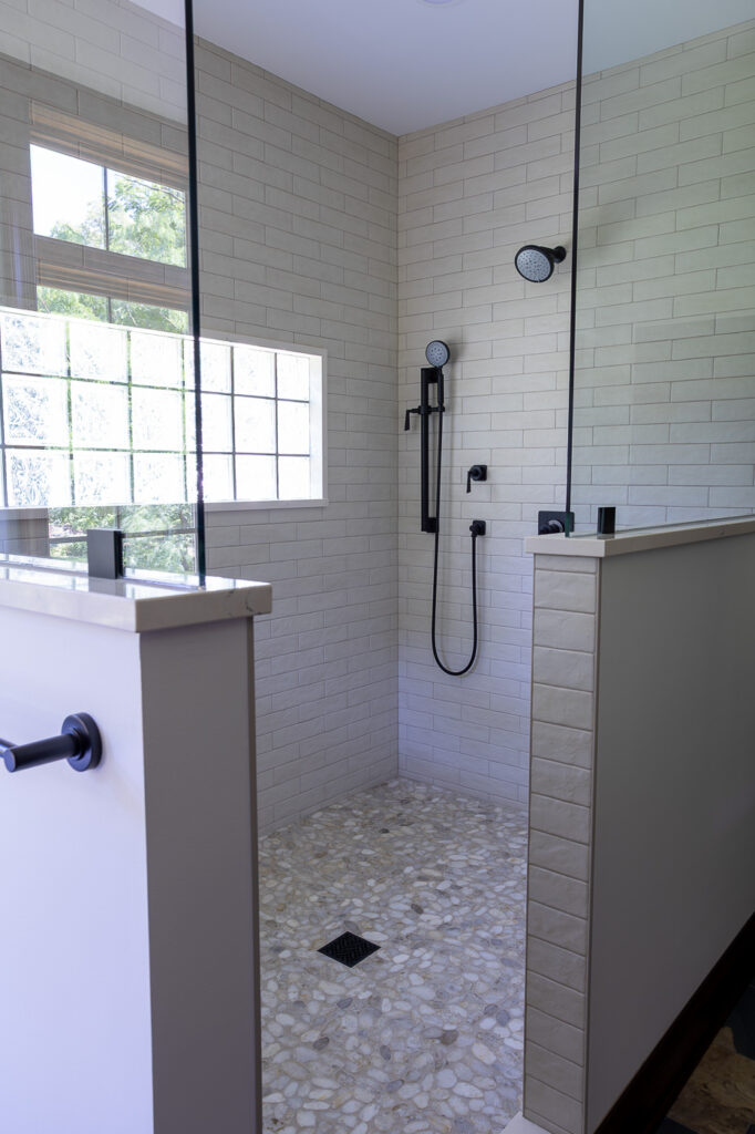 Luxury walk-in shower featuring California Faucets Steampunk Bay fixtures, Ragno Calce 3 x 11 Panna wall tile, The Bati Orient Grey Sliced Polished Pebble shower floor, and Marvin Elevate windows in a master bathroom remodel in Woodstock, Illinois.